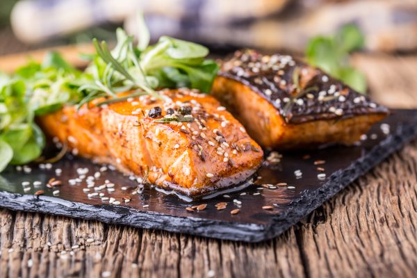 Salmon fillets. Grilled salmon sesame seeds herb decorationon on vintage pan or black slate board. fish roasted on an old wooden table.Studio shot.