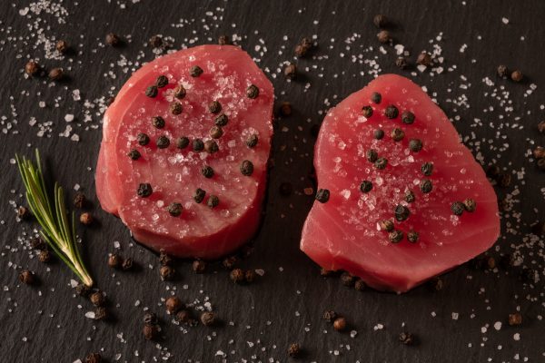 Fresh raw tuna fillet for steak on cutting board with lemon lime salt pepper and spices on dark black rustic background. Tasty fish dinner. Ingredients for cooking