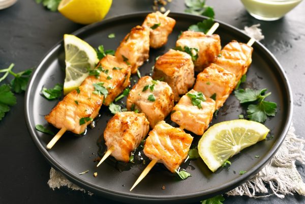 Close up of grilled salmon kebab. Barbecue salmon skewers on black stone background.