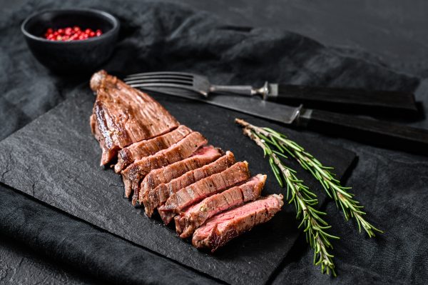 Roasted medium rare sliced flank beef steak. Black background. Top view