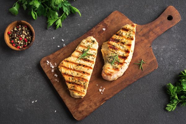 Grilled Chicken or Turkey Breast on black background, top view. Homemade Chicken or Turkey Breast Steak with fresh herbs and spices.